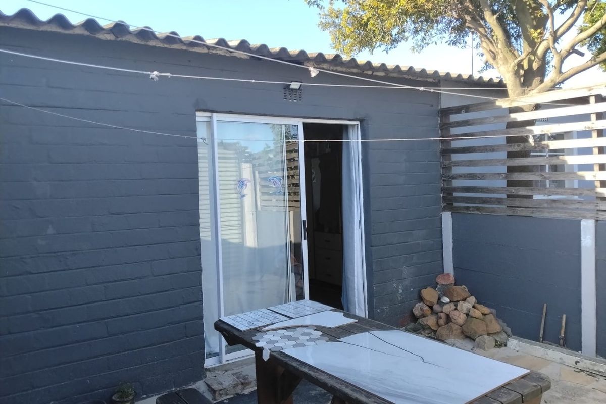 Rear exterior view of the property featuring a painted brick facade, sliding glass door access, and timber slat fencing.