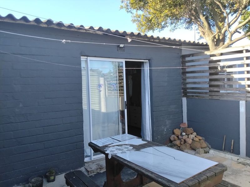 Rear exterior view of the property featuring a painted brick facade, sliding glass door access, and timber slat fencing.
