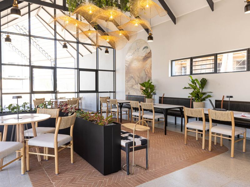 A modern, well-lit clubhouse area featuring high ceilings with exposed rafters, large steel-framed windows, and stylish herringbone flooring with integrated bench seating.