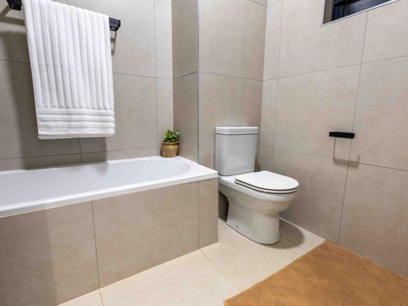 Modern bathroom featuring neutral large-format wall and floor tiles, a built-in bathtub, and a standard toilet with contemporary black fixtures.