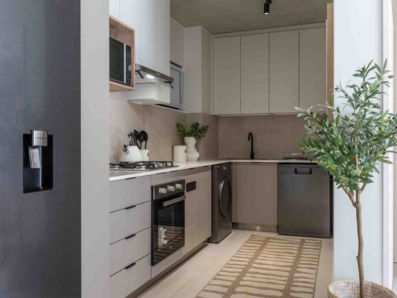 Modern, compact kitchen featuring sleek cabinetry, stone countertops, integrated appliances, and high-quality finishes in a neutral, contemporary palette.