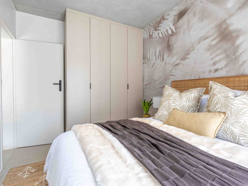 A modern bedroom featuring a built-in wardrobe, textured feature wall, and an exposed concrete ceiling with neutral tiled flooring.