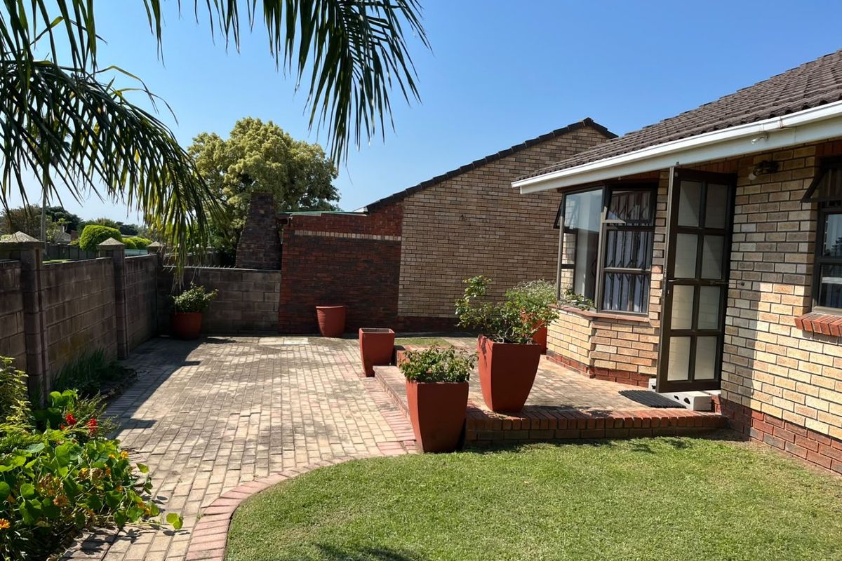 A well-maintained rear exterior featuring brick paving, a neat lawn, and a brick-faced townhouse facade with a tiled roof.