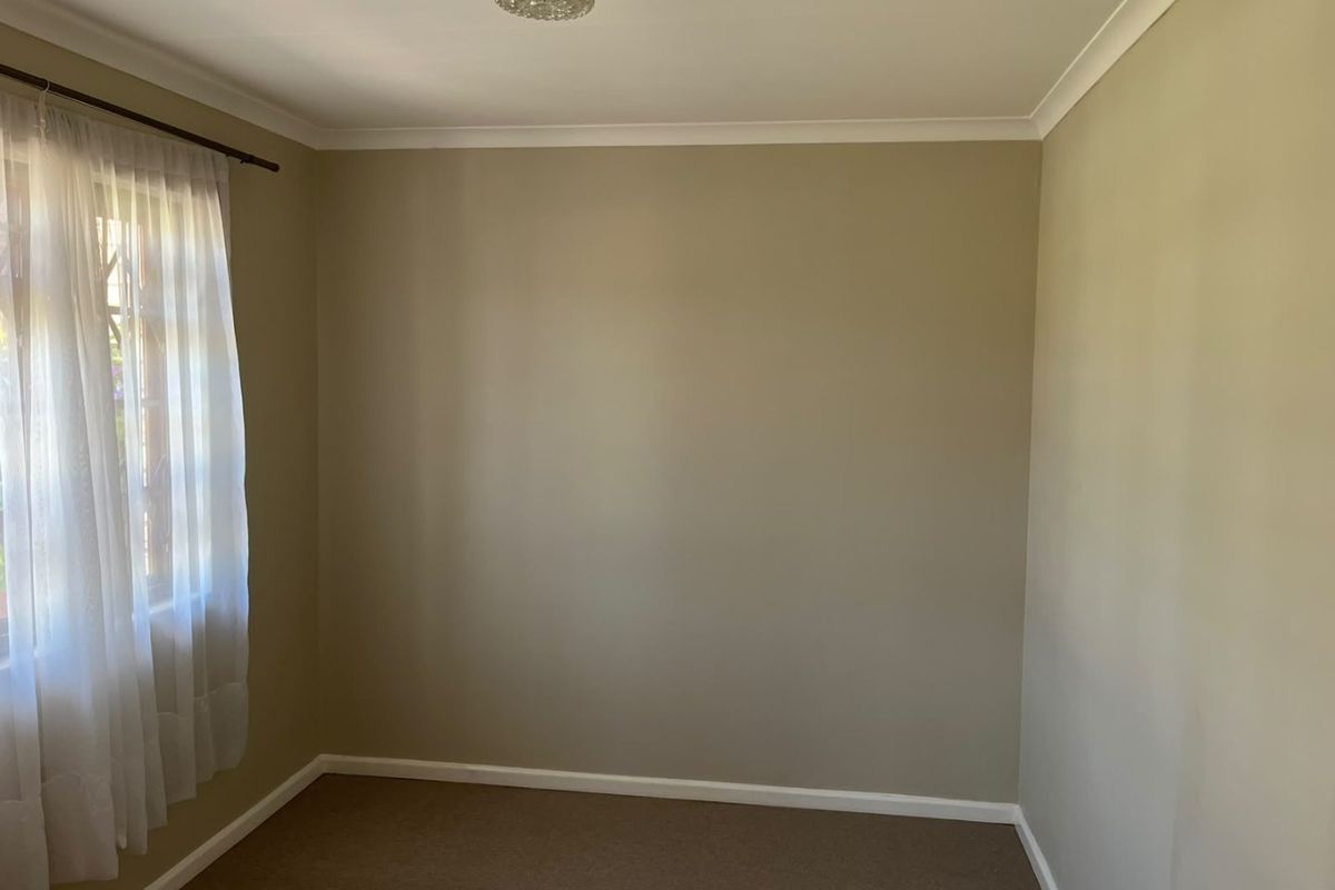 A clean, empty bedroom featuring neutral wall paint, carpeted flooring, and a classic ceiling light fixture, ready for personalization.