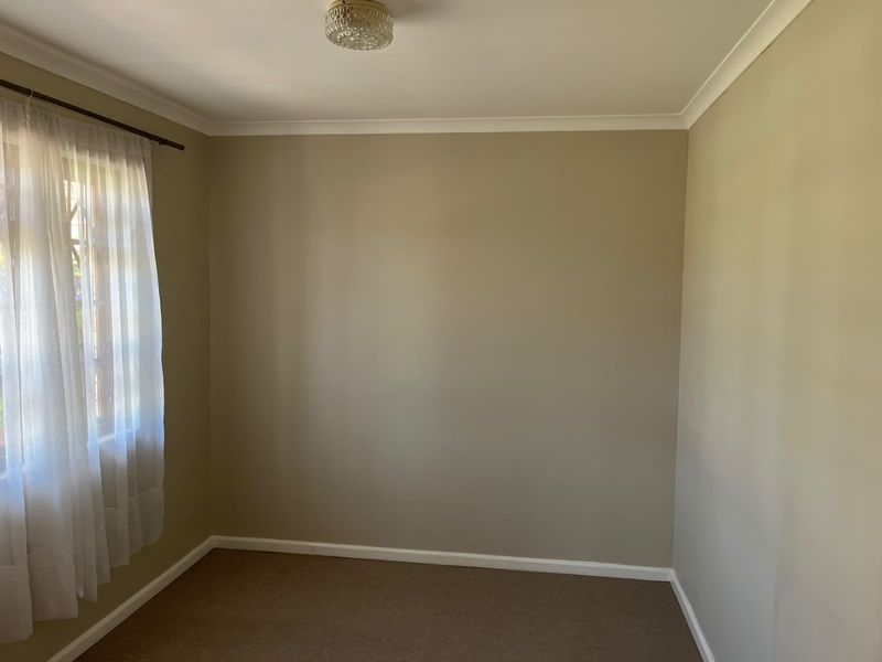 A clean, empty bedroom featuring neutral wall paint, carpeted flooring, and a classic ceiling light fixture, ready for personalization.
