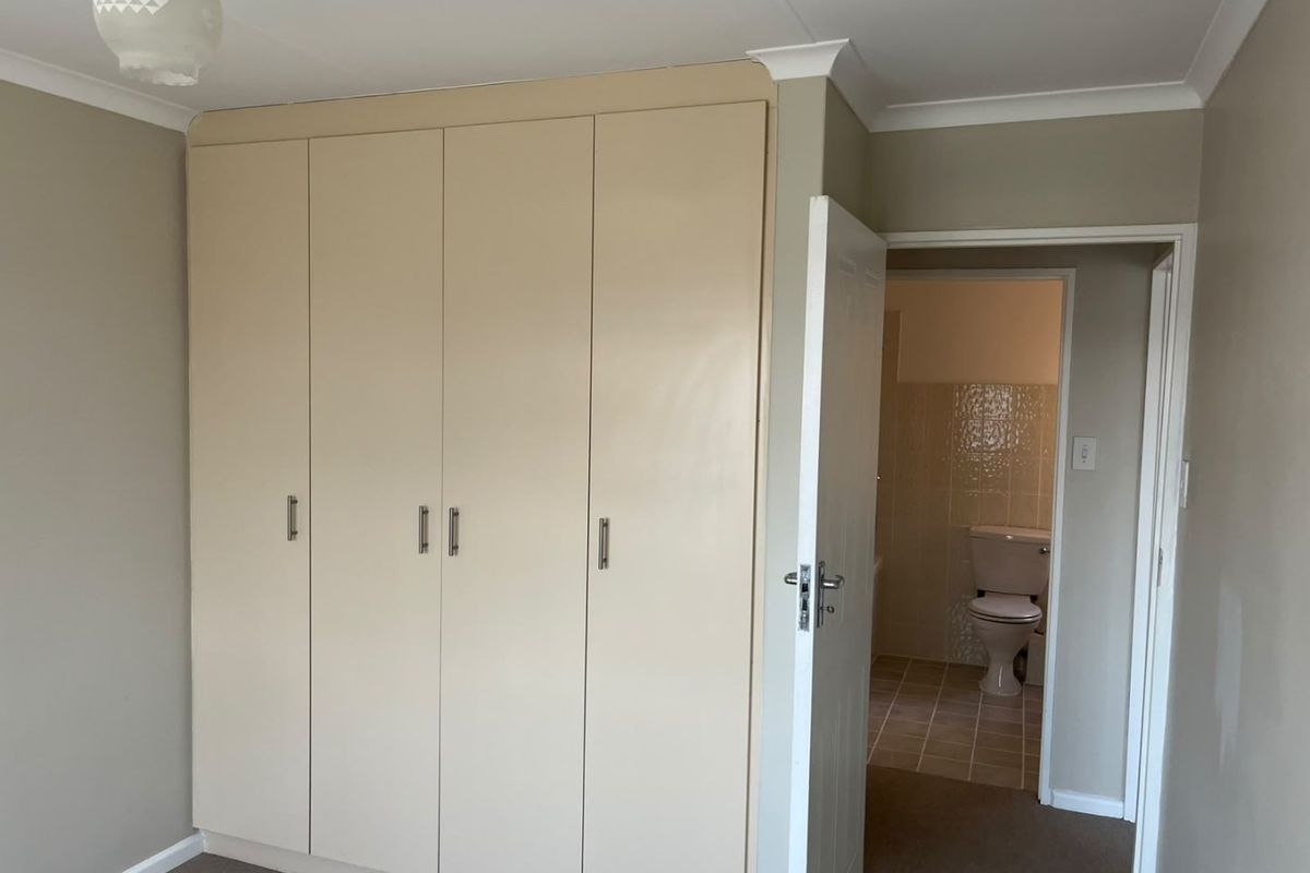 A clean, empty bedroom featuring built-in cupboards and direct access to an en-suite bathroom with tiled flooring.