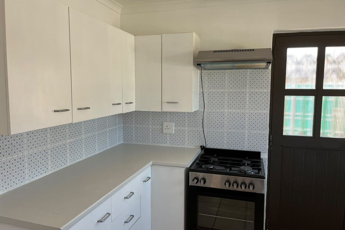 A functional kitchen featuring white cabinetry, tiled backsplash, gas stove with extractor fan, and direct access to the exterior.