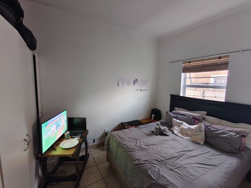A functional bedroom featuring tiled flooring, a built-in wardrobe, and a window with a bamboo blind, providing a comfortable and practical living space.