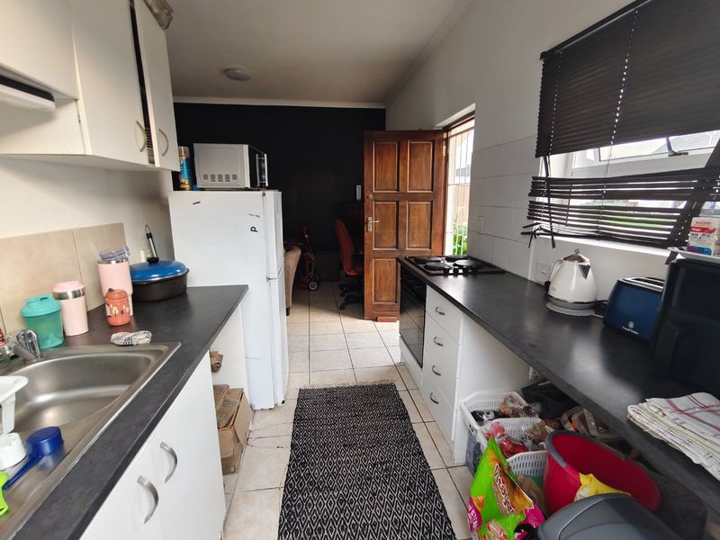 Functional galley-style kitchen featuring built-in cabinetry, dark laminate countertops, integrated oven and hob, and tiled flooring with direct access to an adjacent room.