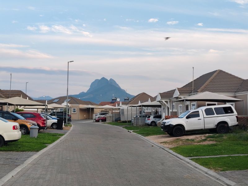 A view of a residential street featuring paved roads, carport structures, and scenic mountain views in the background.