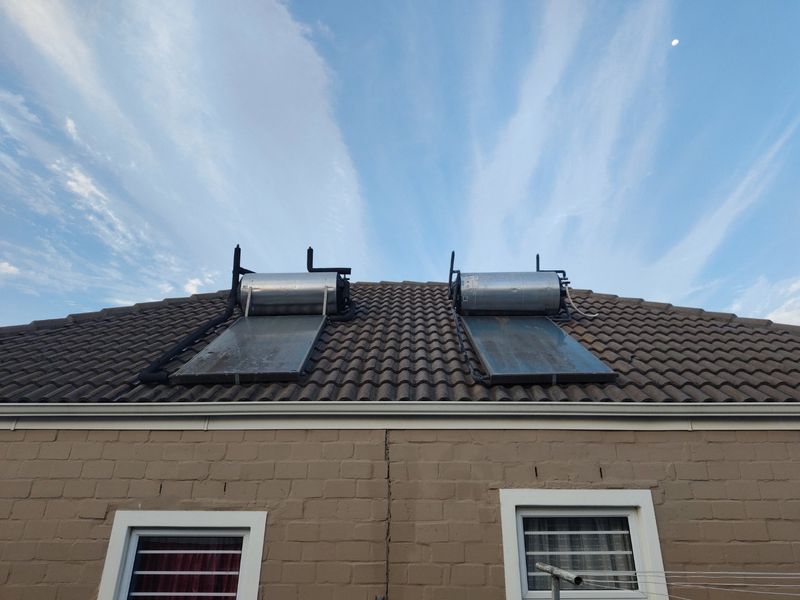 Exterior view of the rear facade featuring two roof-mounted solar water heating units and visible brickwork with a structural crack.