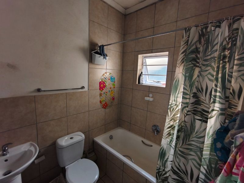 A functional bathroom featuring a bathtub with shower curtain, pedestal basin, and toilet, finished with neutral wall tiling and a louver window.