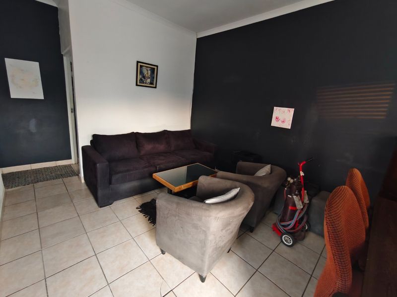 A living room area featuring neutral tiled flooring and contrasting dark accent walls, providing a blank canvas for interior design updates.
