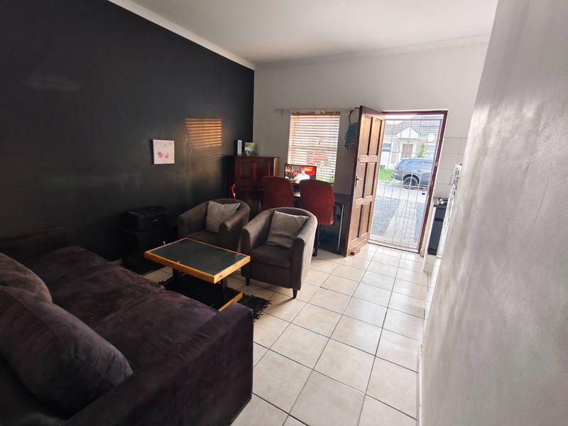 A living room area featuring tiled flooring, a security gate entrance, and a dark accent wall, providing a functional space with direct outdoor access.