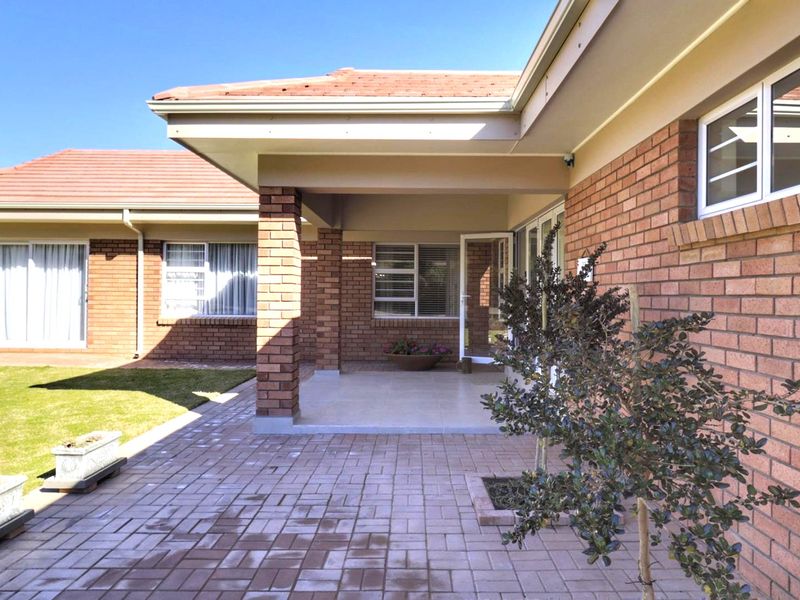A well-maintained covered patio area featuring brick construction, tiled flooring, and direct access to the rear garden and paved outdoor space.