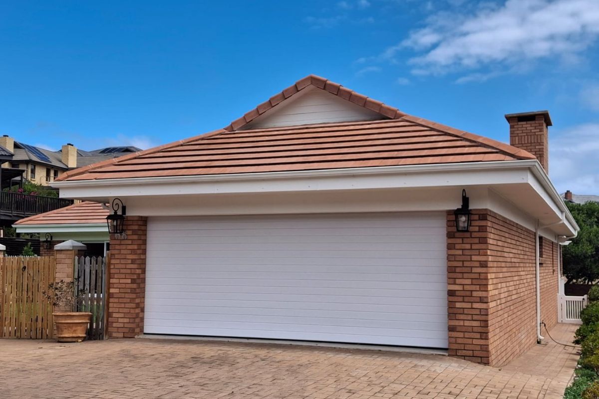 A well-maintained detached brick garage featuring a tiled roof, sectional door, and paved driveway access.