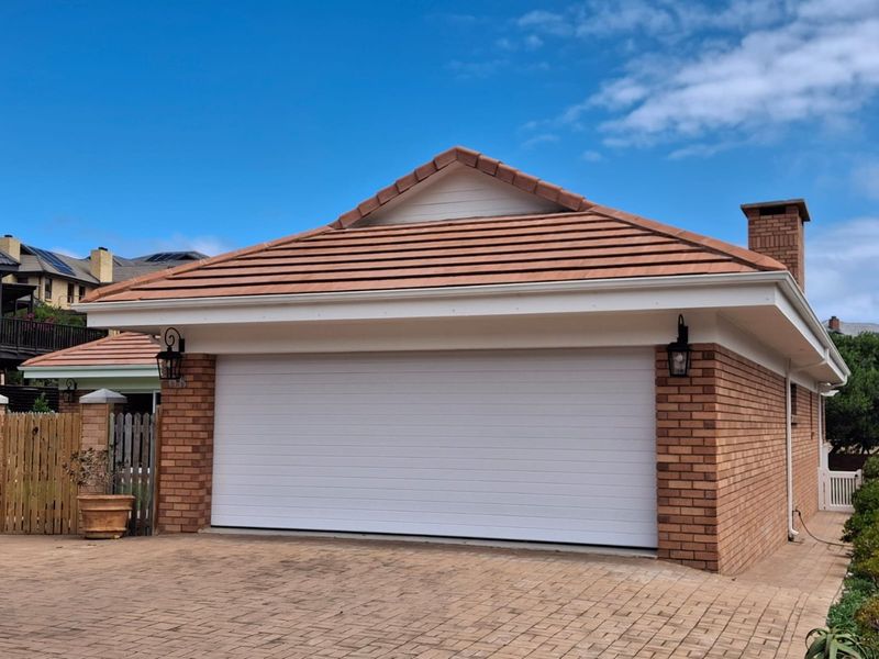 A well-maintained detached brick garage featuring a tiled roof, sectional door, and paved driveway access.