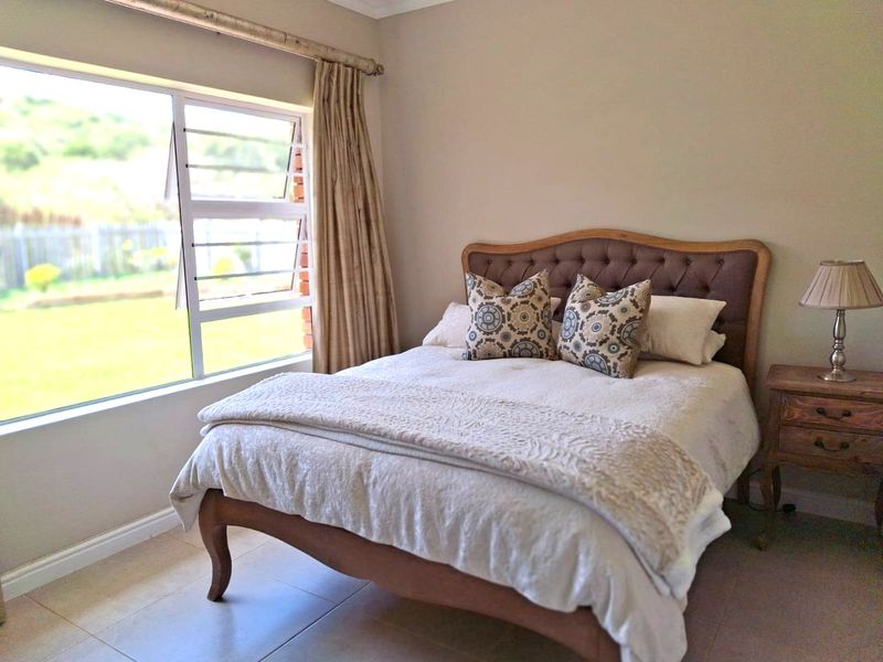 A well-lit bedroom featuring neutral wall tones, tiled flooring, and a large window providing natural light and garden views.
