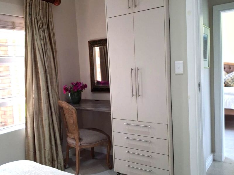A bedroom featuring a tall built-in wardrobe with integrated vanity, neutral wall tones, tiled flooring, and a window with curtain treatments.