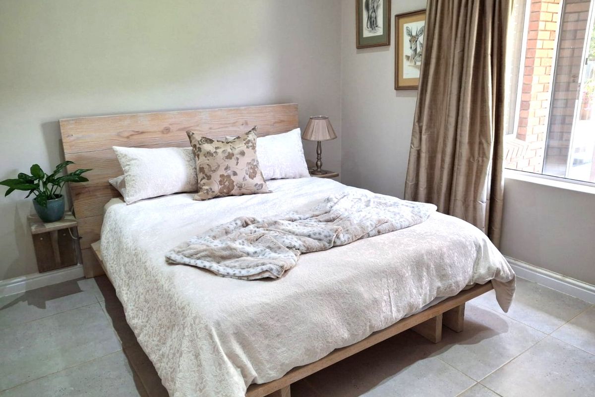 A well-maintained bedroom featuring neutral wall tones, tiled flooring, and a large window allowing for natural light.