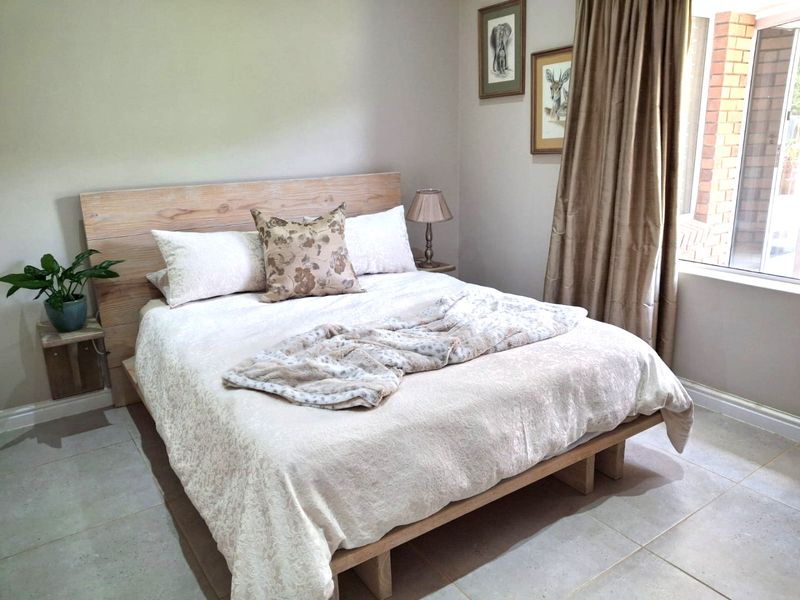 A well-maintained bedroom featuring neutral wall tones, tiled flooring, and a large window allowing for natural light.