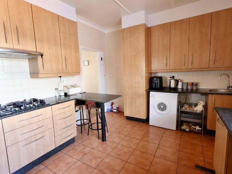 A functional kitchen featuring light wood cabinetry, granite countertops, a gas hob with extractor, and tiled flooring with integrated laundry appliance space.
