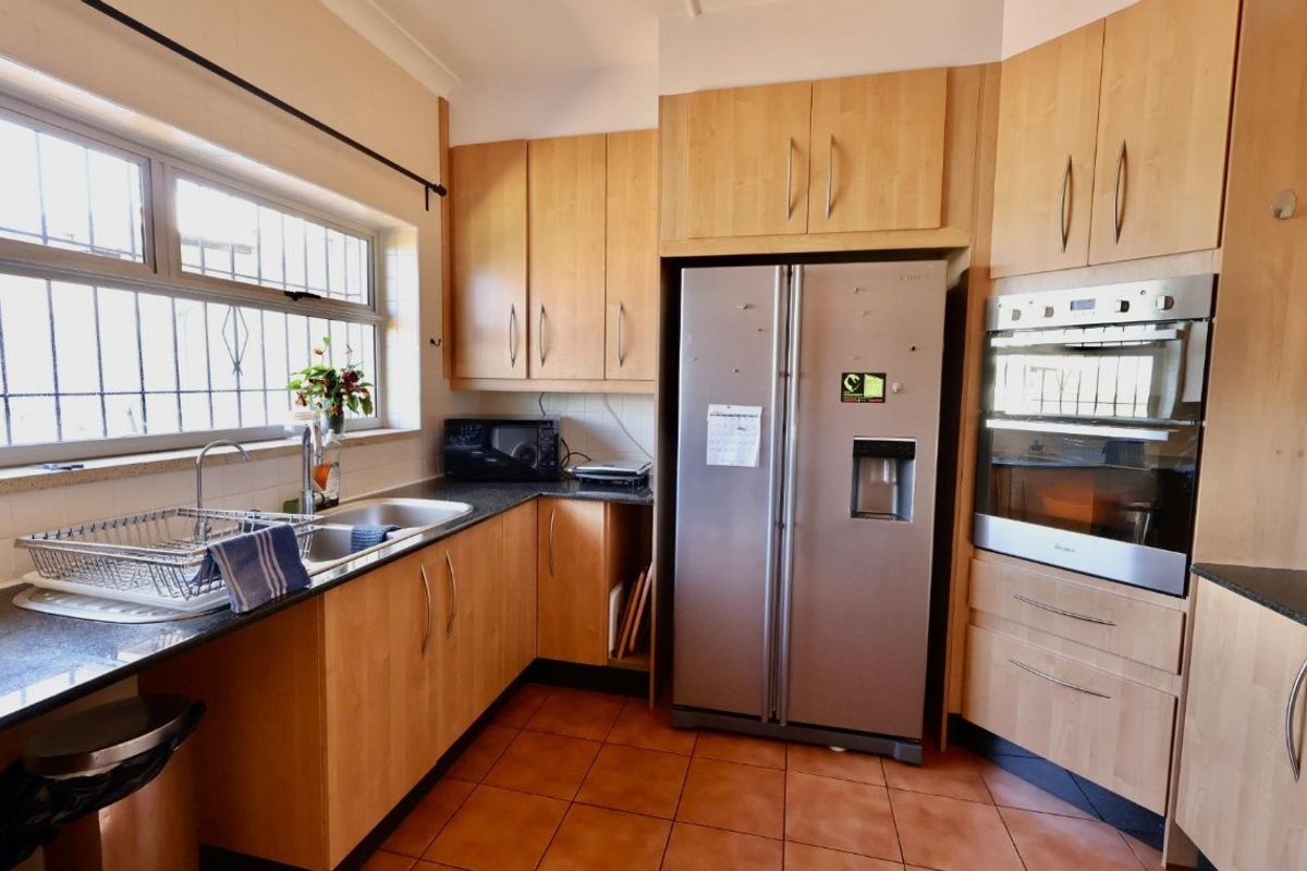 A functional kitchen featuring light wood cabinetry, granite countertops, a double sink, and a built-in double oven with tiled flooring throughout.