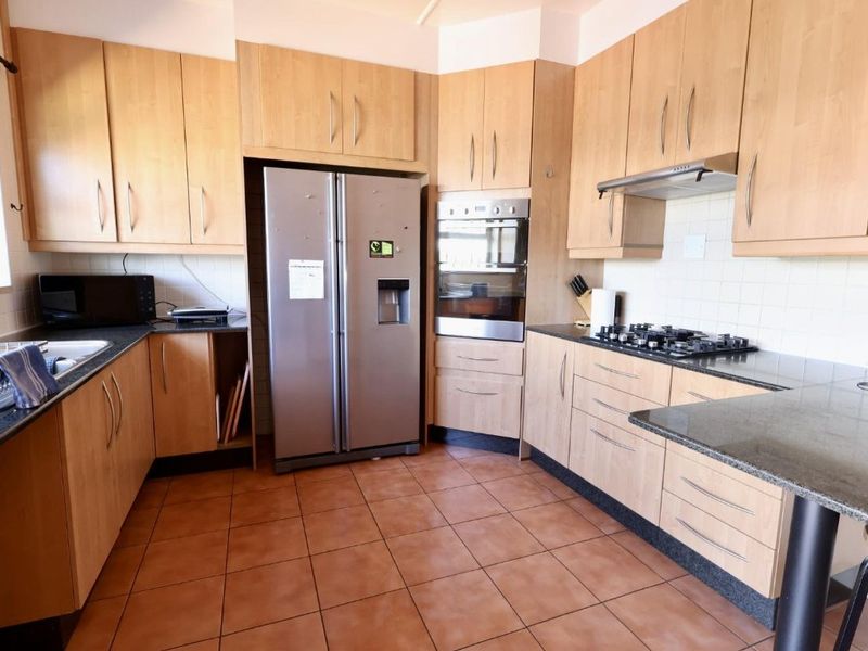 A functional kitchen featuring light wood cabinetry, granite countertops, a gas hob, and built-in oven, finished with tiled flooring.