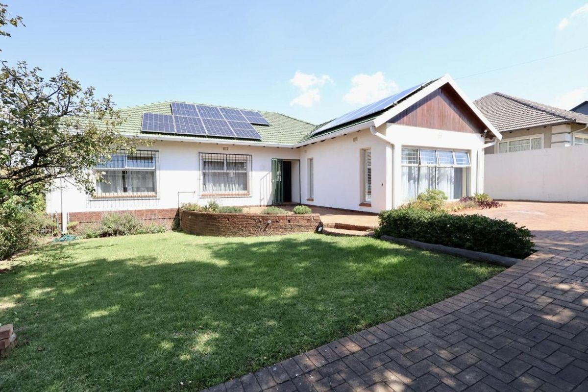 Rear view of the house featuring a well-maintained lawn, brick paved driveway, and roof-mounted solar panels.