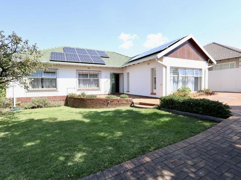 Rear view of the house featuring a well-maintained lawn, brick paved driveway, and roof-mounted solar panels.