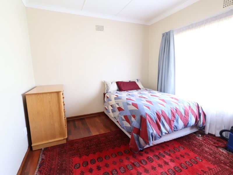 A standard bedroom featuring timber flooring, neutral wall finishes, and a large window allowing for natural light.