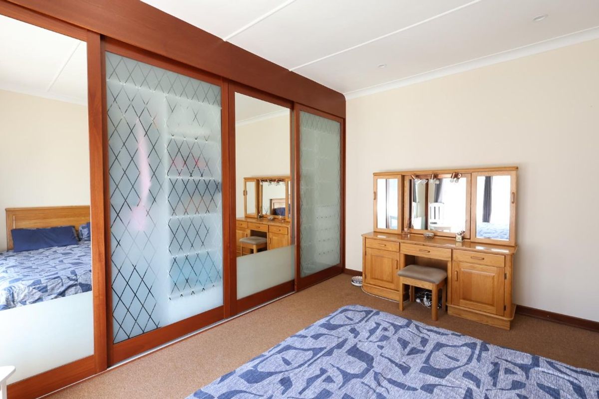 A bedroom featuring a large built-in wardrobe with sliding mirrored and frosted glass doors, neutral walls, and carpeted flooring.