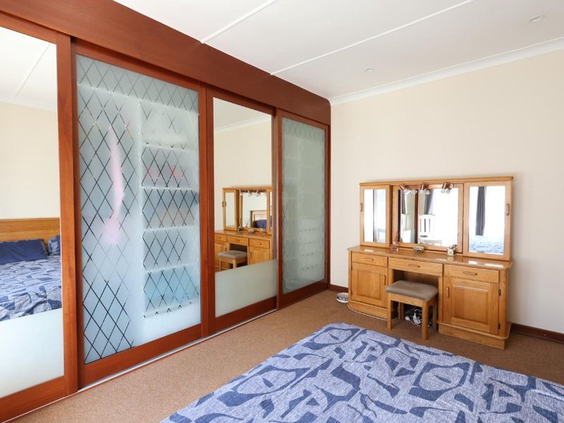 A bedroom featuring a large built-in wardrobe with sliding mirrored and frosted glass doors, neutral walls, and carpeted flooring.