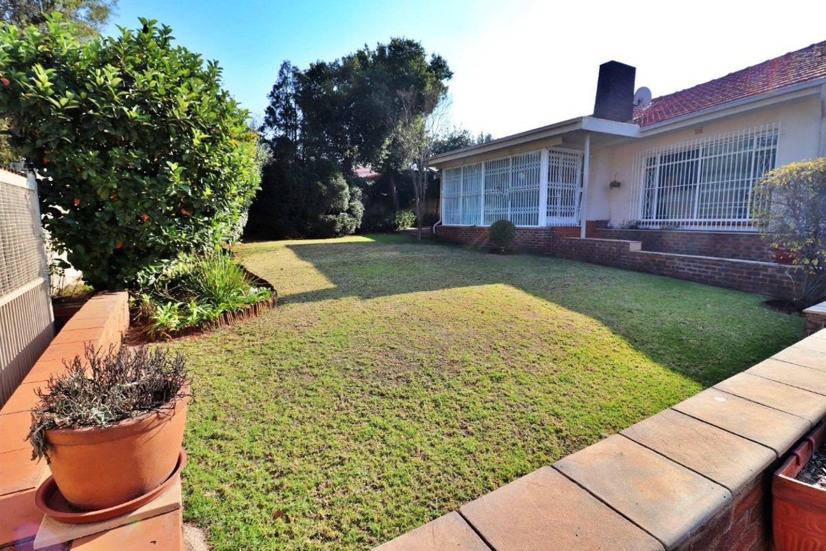 A spacious rear garden featuring a well-maintained lawn, brick retaining walls, and a view of the house exterior with security bars.