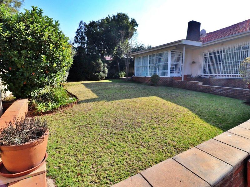 A spacious rear garden featuring a well-maintained lawn, brick retaining walls, and a view of the house exterior with security bars.