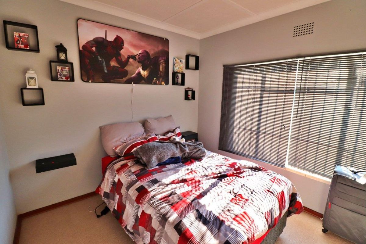 A functional bedroom featuring neutral wall finishes, carpeted flooring, and venetian blinds for light control.