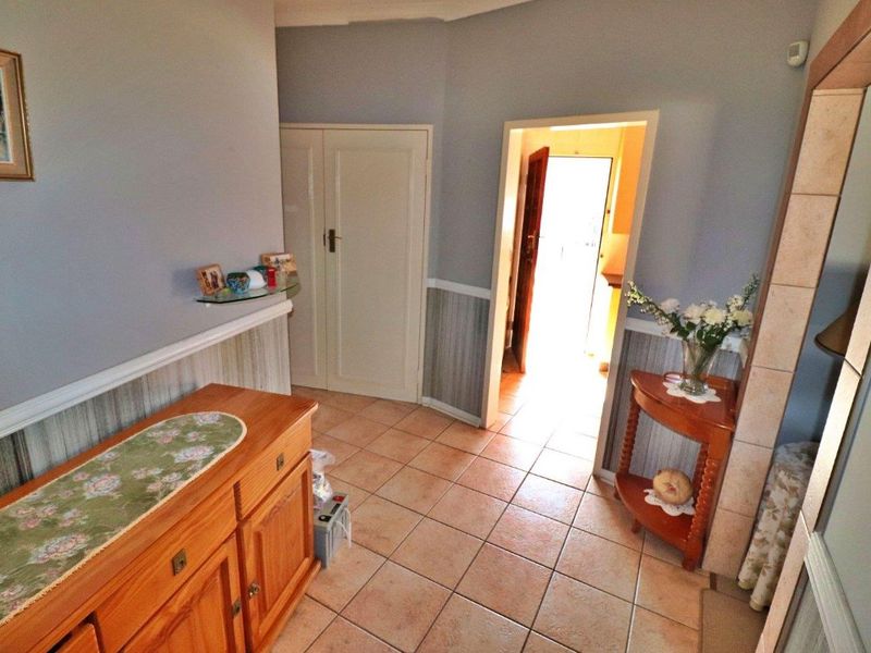 A tiled hallway featuring wainscoting and a built-in cupboard, providing access to adjacent rooms.