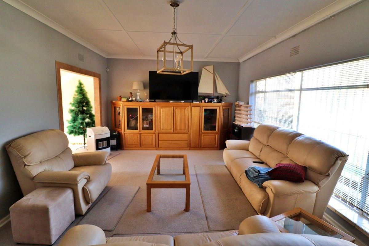 A spacious living room featuring built-in wooden cabinetry, large windows with venetian blinds, and a decorative pendant light fixture.