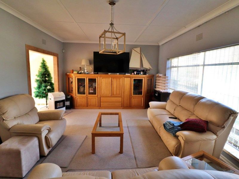 A spacious living room featuring built-in wooden cabinetry, large windows with venetian blinds, and a decorative pendant light fixture.