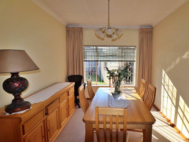 A dining room featuring carpeted flooring, a central light fixture, and a window fitted with security bars.
