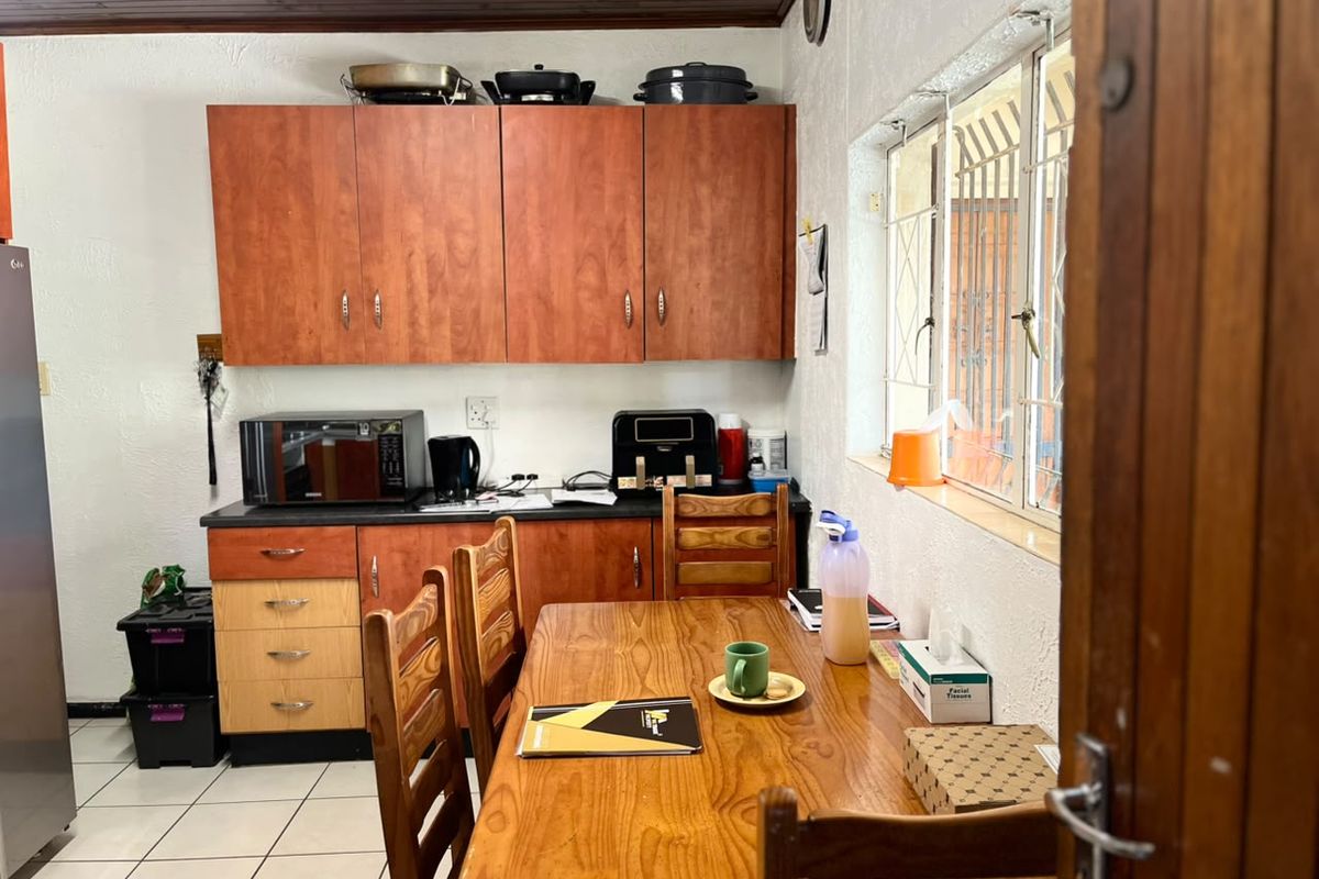A functional kitchen featuring built-in wooden cabinetry, tiled flooring, and a timber ceiling, offering a dated but practical layout.