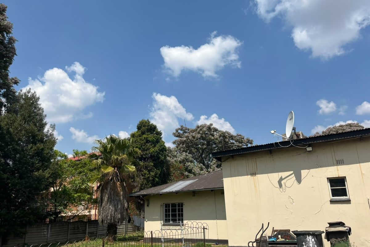 Rear view of the property showing the exterior wall, roof structure, and garden area with perimeter fencing.