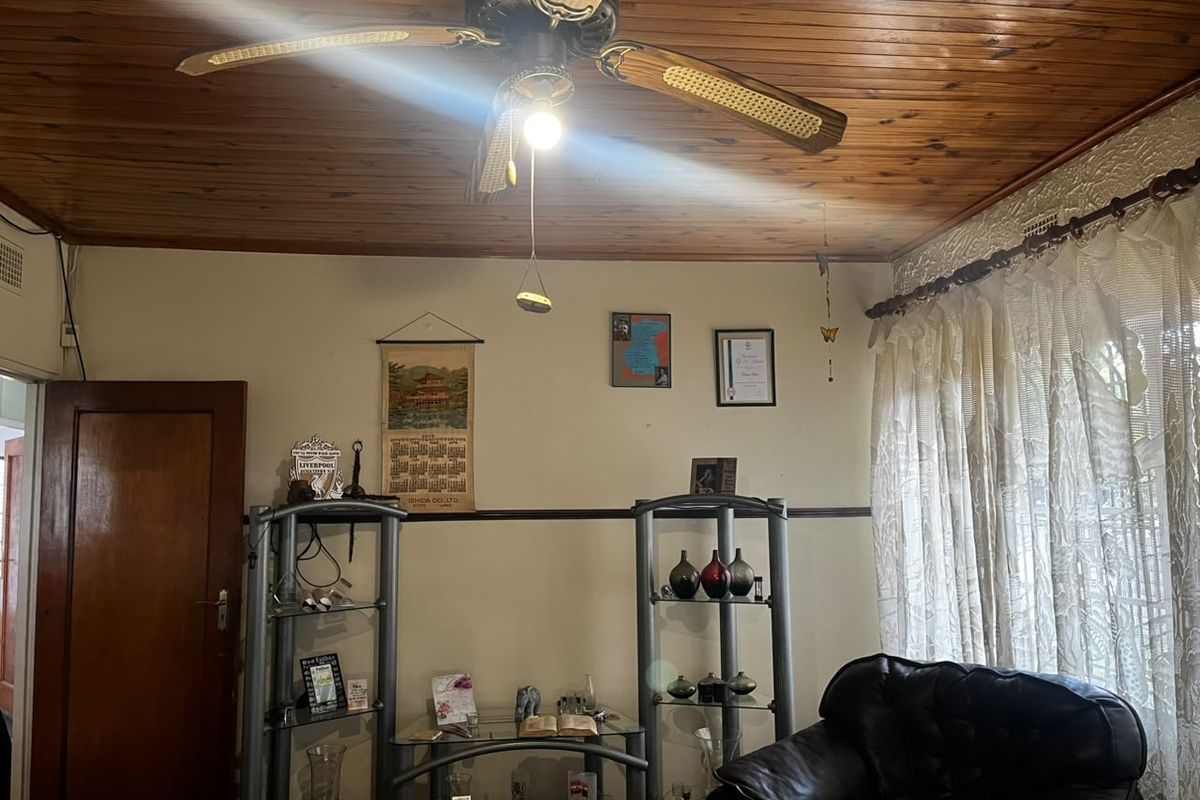 A living room featuring a traditional timber-paneled ceiling, ceiling fan, and classic picture rail detailing, offering a warm and dated aesthetic.