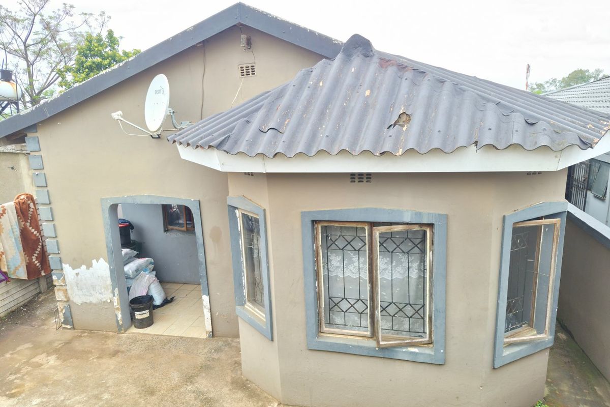 Rear view of a residential property featuring a corrugated roof, security-barred windows, and a paved outdoor area requiring exterior maintenance and painting.