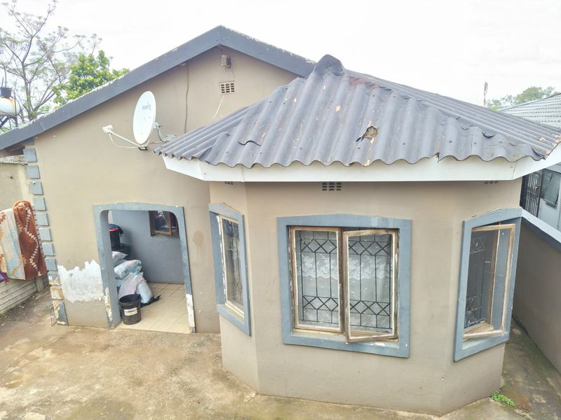 Rear view of a residential property featuring a corrugated roof, security-barred windows, and a paved outdoor area requiring exterior maintenance and painting.