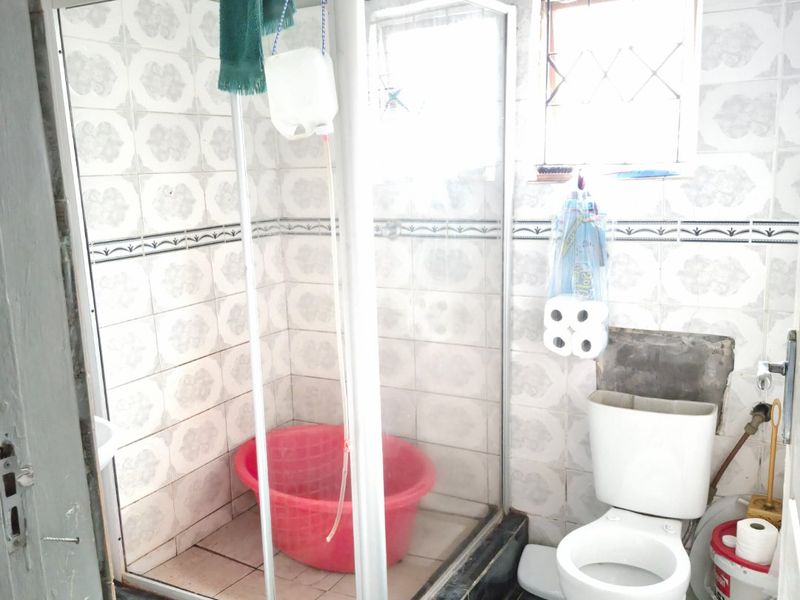 A functional bathroom featuring a shower enclosure, toilet, and tiled finishes. The space shows signs of wear and requires cosmetic updates.