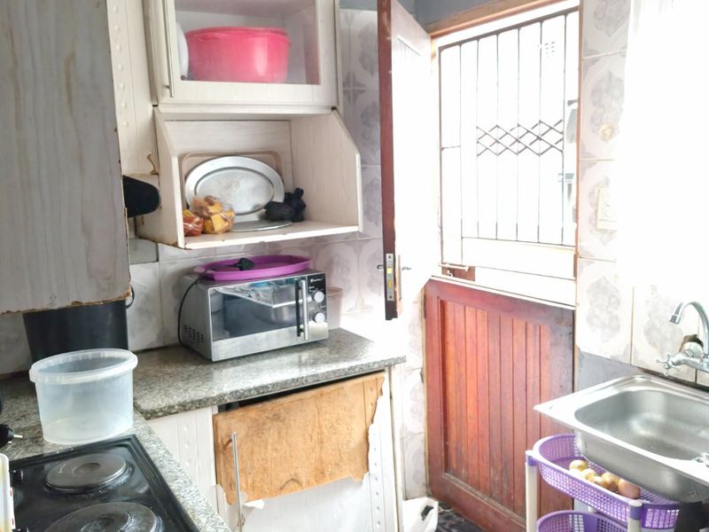 Compact kitchen featuring granite countertops, built-in cabinetry, and an electric hob, with direct access to the exterior via a security-gated door.