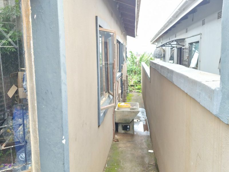 A narrow side passage between two buildings featuring a concrete utility sink, boundary wall, and weathered exterior finishes.
