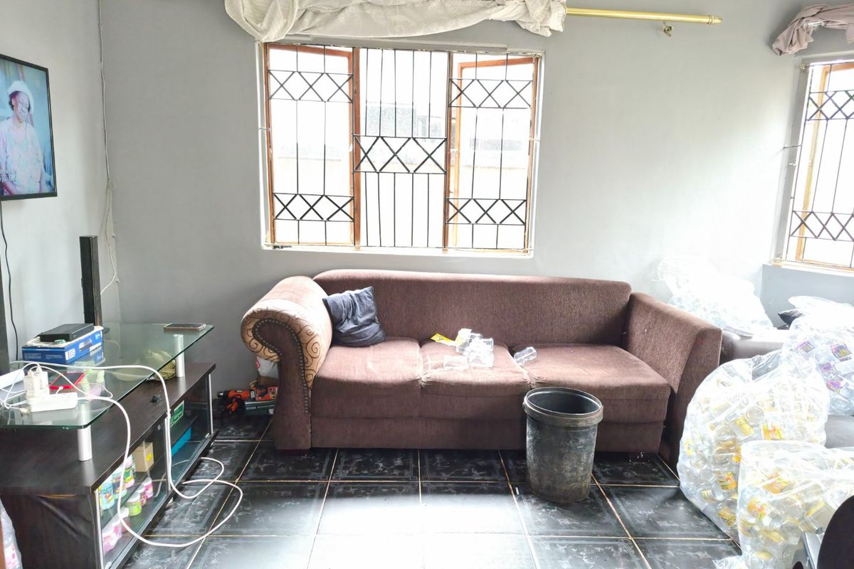 A living room featuring dark tiled flooring and windows fitted with security bars, requiring cosmetic updates to improve the overall aesthetic.
