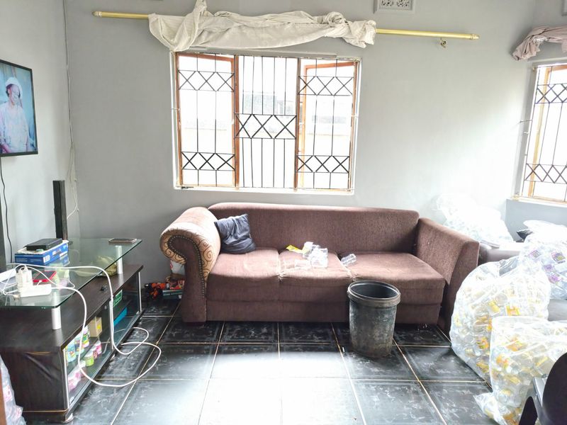 A living room featuring dark tiled flooring and windows fitted with security bars, requiring cosmetic updates to improve the overall aesthetic.